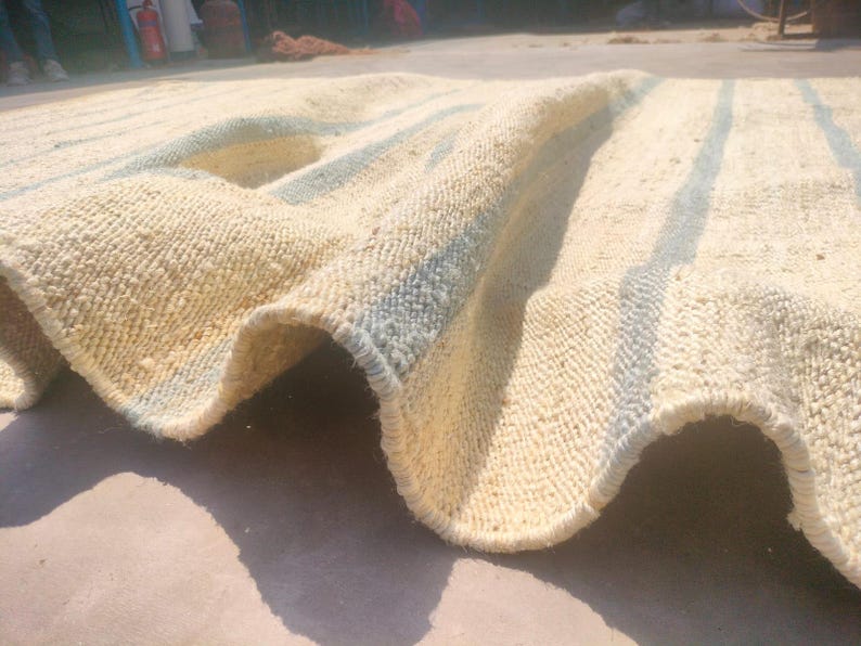 May include: A white and blue striped rug with a woven texture. The rug is folded in half and the blue stripes are visible on the edges.