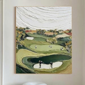 May include: Textured oil painting of a golf course with players. The artwork features a green and tan landscape with white sand traps and a textured white sky. The painting is framed and hangs on a white wall.