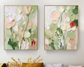 May include: Two abstract floral paintings in a living room setting. The paintings feature a green, white, and pink color scheme with a textured brushstroke style. The paintings are framed in gold and hung on a white wall.