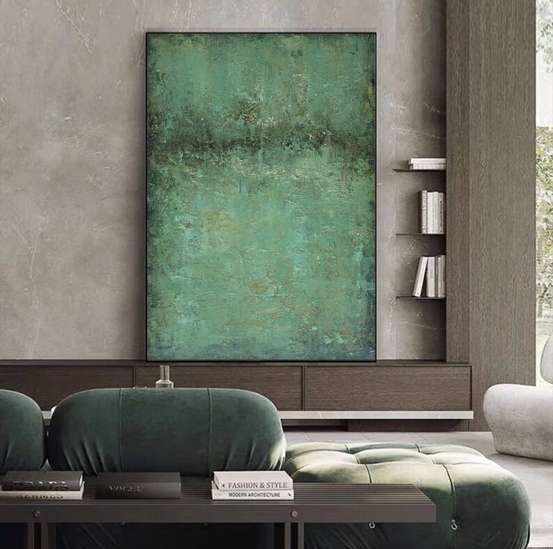 May include: Abstract painting with a green, blue, and brown colour scheme. The painting is framed in black and hangs on a wall in a modern living room.