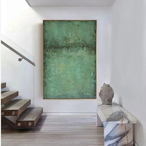 May include: Abstract painting with a green and brown colour scheme. The painting is framed and hanging on a white wall in a modern home.