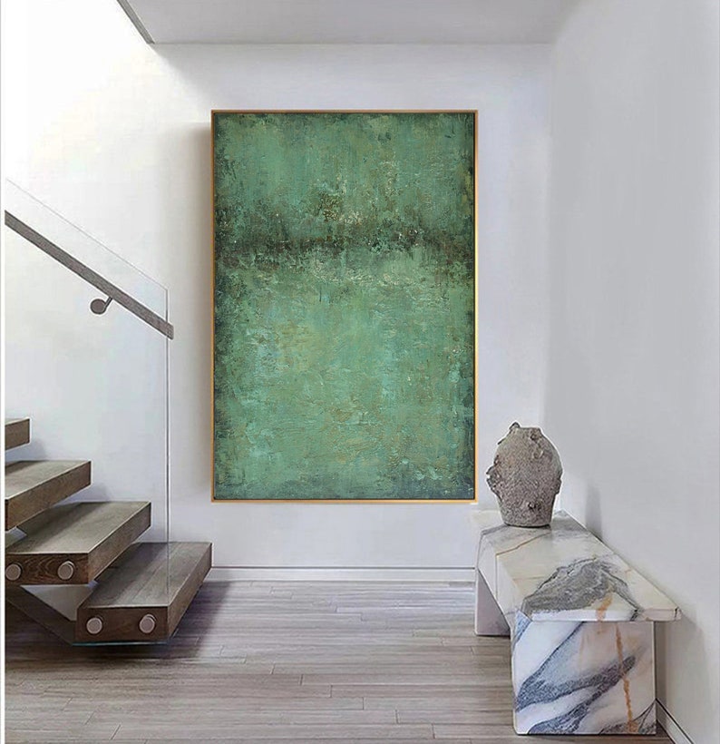 May include: Abstract painting with a green and brown colour scheme. The painting is framed and hanging on a white wall in a modern home.