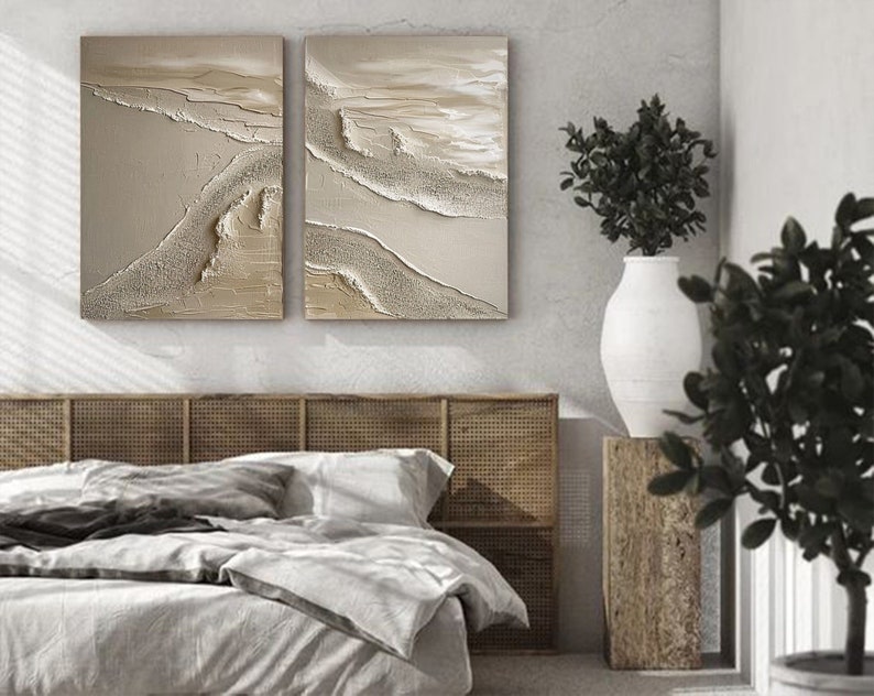 May include: Two abstract paintings with a beige and white color scheme. The paintings are hung on a wall above a bed with a woven headboard.