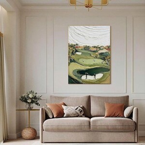 May include: An abstract golf course painting with a textured, layered effect. The artwork features a green golf course with players, sand traps, and trees. The sky is white with textured brushstrokes. The painting is displayed above a beige sofa with orange and patterned pillows.