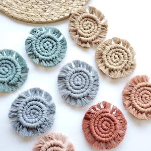 May include: Set of eight round woven coasters in various colors, including beige, blue, green, and orange. Each coaster has a fringe border and a spiral design in the center.