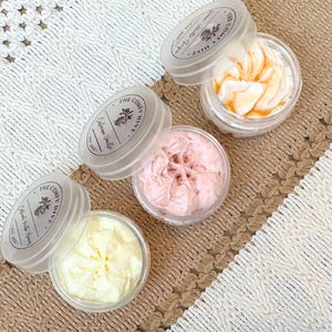 May include: Three small jars of whipped body butter with lids. The jars are labeled "The Country Hive" and have different scents: "French Vanilla", "Honey Apple", and "Blood Milk Honey".