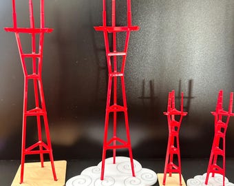 Puede incluir: Cuatro torres rojas en miniatura de diferentes alturas, con un diseño arquitectónico distintivo. Están montadas sobre bases de madera o plataformas blancas con forma de nube. Las estructuras tienen una estructura de celosía.