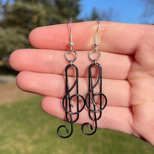 May include: A pair of black wire earrings shaped like treble clefs. The earrings are hanging from silver hooks.