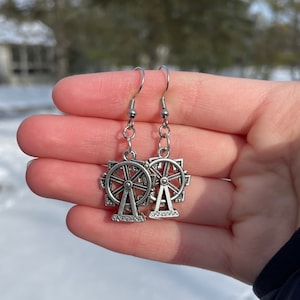 May include: Silver earrings with a Ferris wheel design. The earrings are dangling and have a silver chain.