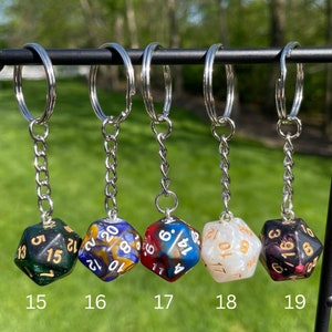 May include: Five different keychains with dice charms. The dice are multi-colored and have white numbers. The keychains are silver.