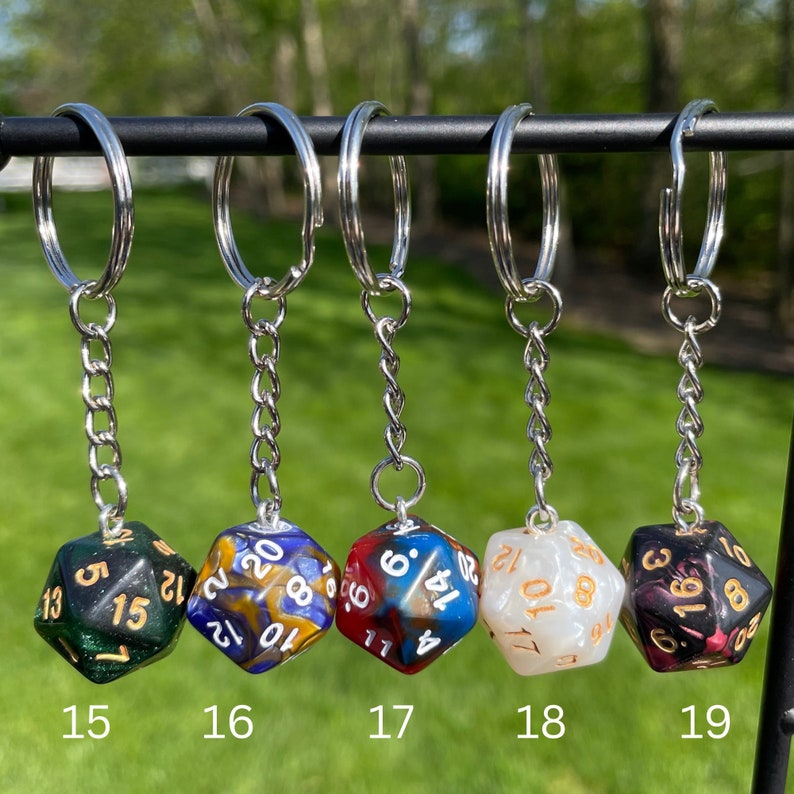 May include: Five different keychains with dice charms. The dice are multi-colored and have white numbers. The keychains are silver.