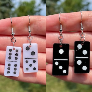 May include: A pair of dangle earrings featuring black and white domino tiles. The domino tiles are printed with white dots on a black background and black dots on a white background.