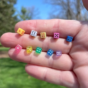 May include: A set of ten small dice in various colors, including yellow, pink, blue, green, and purple. The dice are all translucent and have black dots on them.