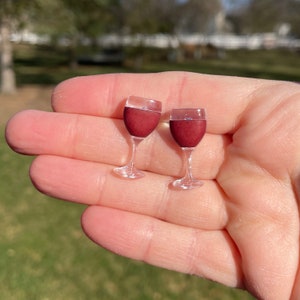 May include: A pair of red wine glass earrings. The earrings are made of clear plastic and have a realistic design.