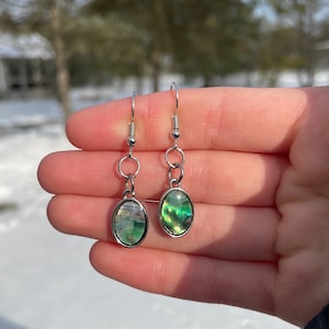 May include: A pair of silver dangle earrings with oval-shaped green and iridescent abalone shell accents.