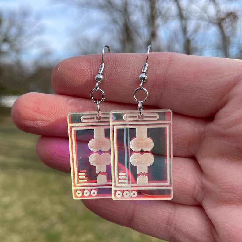 May include: A pair of iridescent earrings with a design of a computer screen displaying a pair of bones. The earrings are silver and have a hook closure.