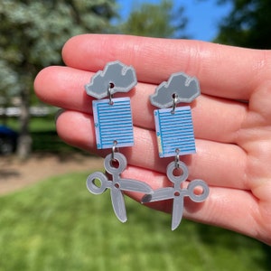 May include: Gray cloud earrings with a blue and white patterned paper clip and gray scissors dangling below.