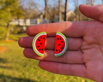 Könnte beinhalten: Ein Paar Wassermelonen-Ohrringe mit grünen und roten Akzenten. Die Ohrringe werden auf einer Hand gezeigt.