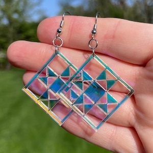 May include: A pair of iridescent blue and green geometric earrings with silver hooks. The earrings are made of clear acrylic and have a geometric pattern.