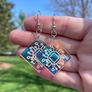 May include: A pair of iridescent silver earrings with a diamond-shaped design featuring a white circuit board pattern.
