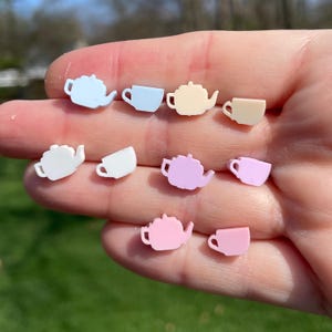 May include: A set of eight pastel-colored teapot and cup earrings. The earrings are made of plastic and are shaped like teapots and cups. The colors of the earrings are light blue, light pink, white, and yellow.