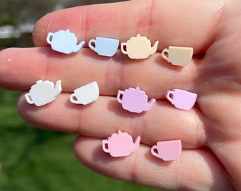 May include: A set of eight pastel-colored teapot and cup earrings. The earrings are made of plastic and are shaped like teapots and cups. The colors of the earrings are light blue, light pink, white, and yellow.