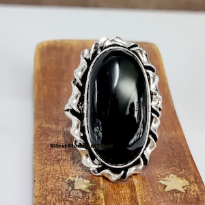 May include: A silver ring with a large, oval-shaped black onyx stone. The ring has a detailed, ornate design around the stone.