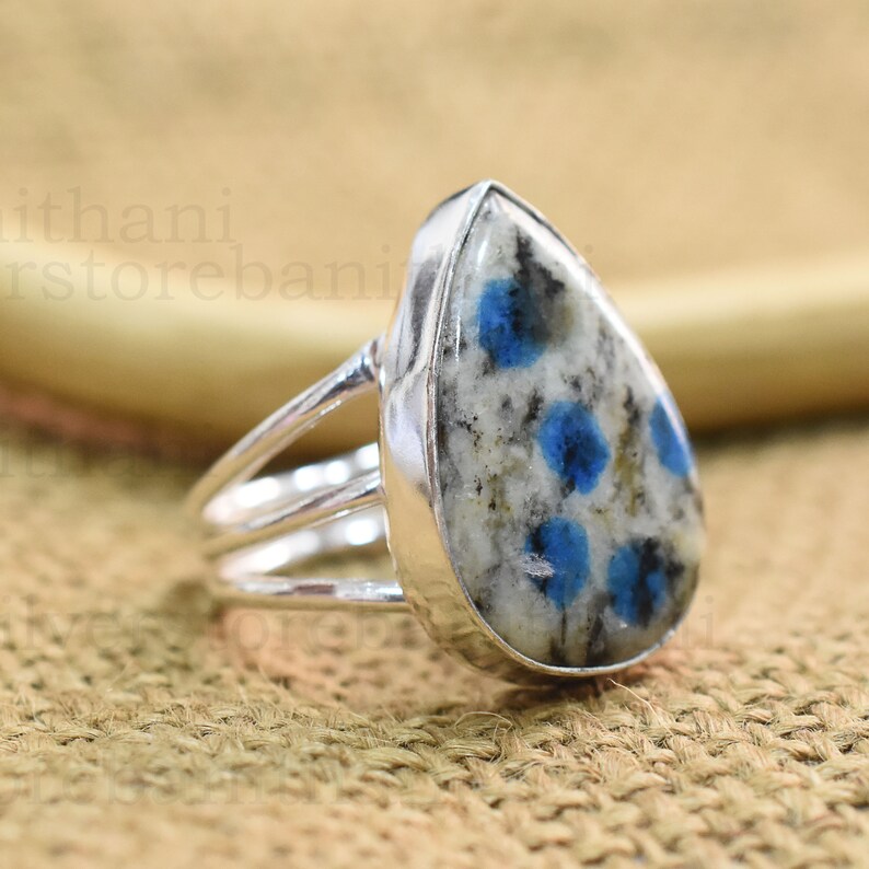 May include: A silver ring with a pear-shaped blue and white gemstone. The gemstone has a speckled pattern of blue and white.