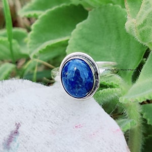 Könnte beinhalten: Ein silberner Ring mit einem blauen, ovalen Lapislazuli-Stein. Der Ring hat ein schlichtes Design mit einem glatten Band und einer Zargenfassung für den Stein.