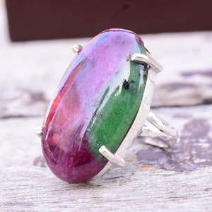 Puede incluir: Un anillo de plata con una gran piedra preciosa ovalada de color verde y rosa. La piedra está engastada en un engaste de garras de plata.