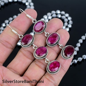 Könnte beinhalten: Ein Paar silberne Ohrringe mit rosafarbenen ovalen Edelsteinen. Jeder Ohrring hat drei Edelsteine, wobei der oberste Edelstein der größte ist. Die Ohrringe haben ein schlichtes Design mit einem seilartigen Rand um jeden Edelstein.