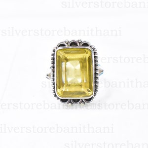 Può includere: Un anello d'argento con una grande pietra preziosa gialla rettangolare. La pietra preziosa è incastonata in una cornice d'argento ornata con un bordo di perline. L'anello è mostrato su sfondo bianco.
