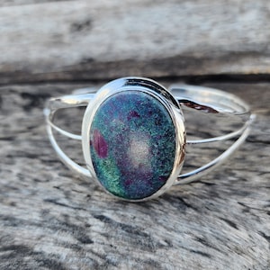 May include: A silver bangle bracelet with a green and pink oval gemstone set in the center.