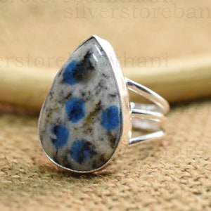 May include: A silver ring with a teardrop-shaped blue and white gemstone. The gemstone has a speckled pattern with blue spots.