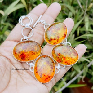 Peut inclure: Un bracelet en argent avec quatre pierres d'ambre de forme ovale. Les pierres d'ambre sont un mélange de couleurs jaunes, orange et brun avec des inclusions. Le bracelet a un fermoir en T.