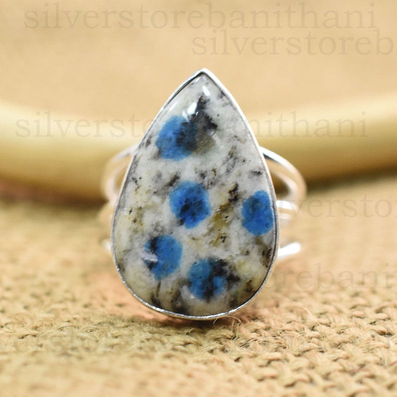 May include: A silver ring with a pear-shaped blue and white gemstone. The gemstone has a speckled pattern with blue spots.