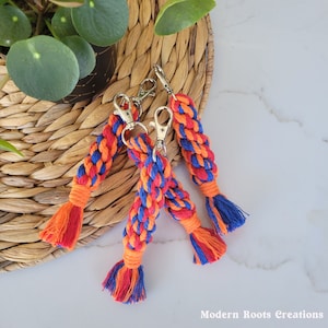 May include: Three colorful keychains made of braided rope with orange, blue, and red colors. The keychains have silver key rings and tassels at the end.