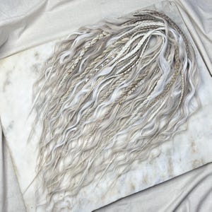 May include: A set of white and light blonde synthetic hair extensions with a wavy texture. The extensions are arranged in a loose, flowing style.