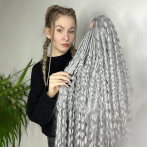 Op de afbeelding: Een lange, dikke set zilvergrijze synthetische haarverlengingen met een krullende textuur.