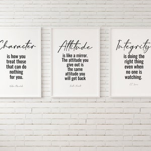 May include: Three white framed prints with black text on a white brick wall. The prints feature quotes about character, attitude, and integrity. The quote about character reads "Character is how you treat those that can do nothing for you." by  John Ruskin. The quote about attitude reads "Attitude is like a mirror. The attitude you give out is the same attitude you will get back." by  Dale Carnegie. The quote about integrity reads "Integrity is doing the right thing even when no one is watching." by C.S. Lewis.