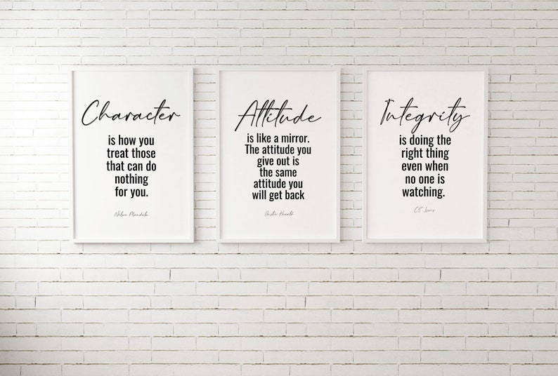 May include: Three white framed prints with black text on a white brick wall. The prints feature quotes about character, attitude, and integrity. The quote about character reads "Character is how you treat those that can do nothing for you." by  John Ruskin. The quote about attitude reads "Attitude is like a mirror. The attitude you give out is the same attitude you will get back." by  Dale Carnegie. The quote about integrity reads "Integrity is doing the right thing even when no one is watching." by C.S. Lewis.