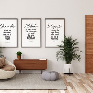 May include: Three framed inspirational quotes on a white wall with a brown door, a brown armchair, a wooden table, and two potted plants. The quotes are "Character is how you treat those that can do nothing for you." "Attitude is like a mirror. The attitude you give out is the same attitude you will get back." "Integrity is doing the right thing even when no one is watching."