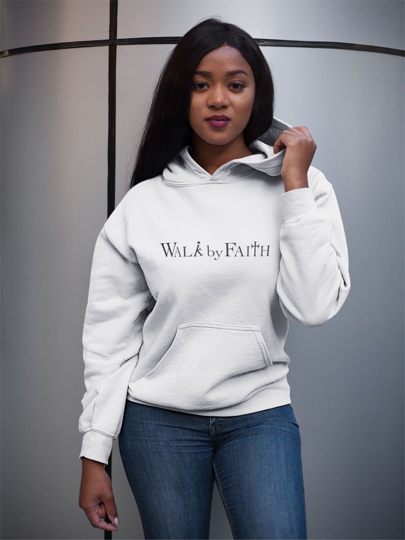 Op de afbeelding: Een wit hoodie met de tekst "WALK by FAITH" erop gedrukt. Het model draagt de hoodie met een blauwe jeans.