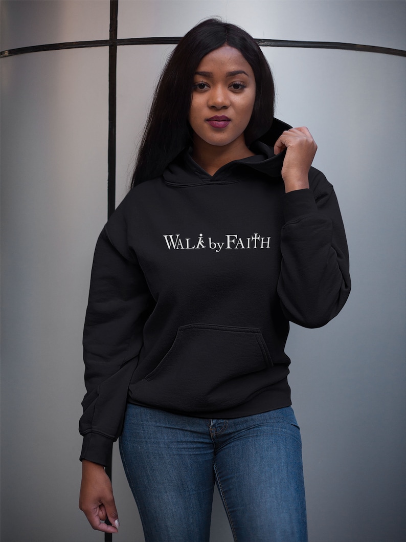 Op de afbeelding: Een zwarte hoodie met een witte afbeelding met de tekst "WALK by FAITH".