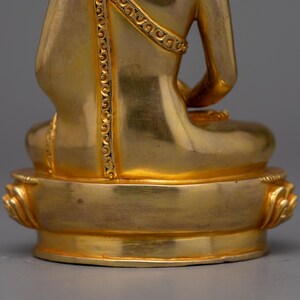 May include: A gold-colored statue of a seated Buddha, with intricate details on the robe and base. The statue is made of metal and has a smooth, polished finish.