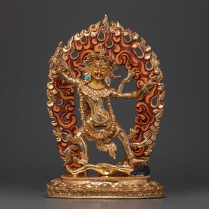 Könnte beinhalten: Eine goldfarbene Statue einer Gottheit mit einem grimmigen Ausdruck, die in einem feurigen Heiligenschein steht. Die Statue ist mit komplizierten Details und bunten Edelsteinen verziert.