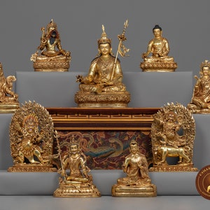 May include: A collection of nine gold-colored statues of deities and figures, arranged on a tiered platform. The statues are intricately detailed and feature various poses and expressions. The statues are displayed on a wooden platform with a decorative design.