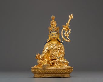 May include: A golden statue of a seated figure, adorned with a crown and intricate detailing. The figure holds a ceremonial object and is seated on a detailed base. The statue has blue and red accents.