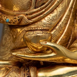 K&ouml;nnte beinhalten: Nahaufnahme einer goldenen Hand einer Statue, die eine kleine, runde, goldene Schale h&auml;lt. Die Schale hat komplizierte Details und eine glatte, polierte Oberfl&auml;che.