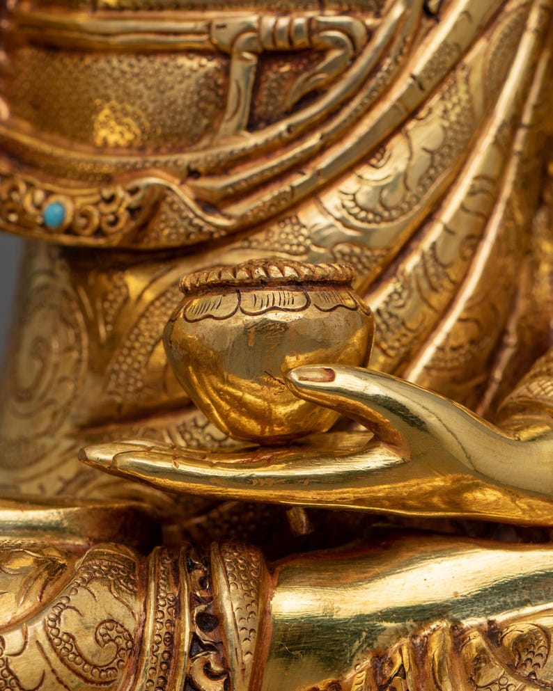 K&ouml;nnte beinhalten: Nahaufnahme einer goldenen Hand einer Statue, die eine kleine, runde, goldene Schale h&auml;lt. Die Schale hat komplizierte Details und eine glatte, polierte Oberfl&auml;che.